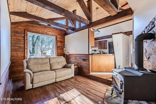 living room with vaulted ceiling with beams, wood ceiling, a wood stove, and light hardwood / wood-style flooring