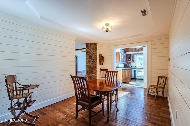 dining room featuring a raised ceiling, dark hardwood / wood-style floors, and wood walls