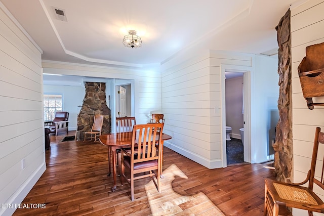 dining room with dark hardwood / wood-style flooring, wooden walls, and a tray ceiling