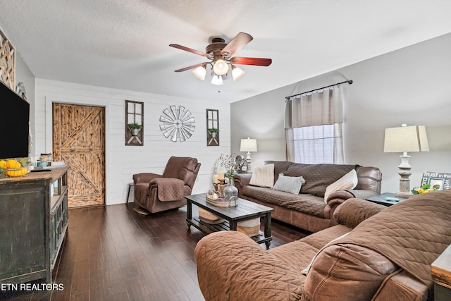 living room with a textured ceiling, ceiling fan, dark hardwood / wood-style flooring, and a barn door