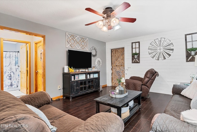 living room with a textured ceiling, dark hardwood / wood-style floors, wood walls, and ceiling fan