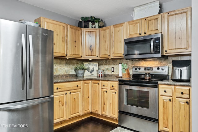 kitchen with light brown cabinetry, appliances with stainless steel finishes, decorative backsplash, and dark stone counters