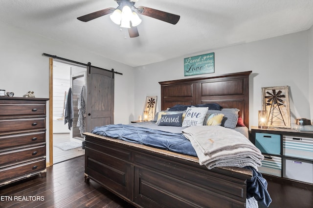 bedroom featuring ceiling fan, a barn door, dark hardwood / wood-style flooring, and a textured ceiling