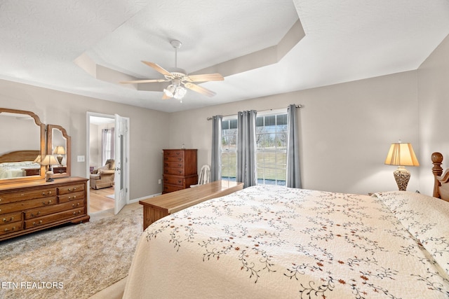 bedroom with a raised ceiling, ceiling fan, and light carpet