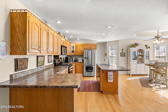 kitchen featuring stainless steel appliances, an island with sink, sink, ceiling fan, and light hardwood / wood-style flooring