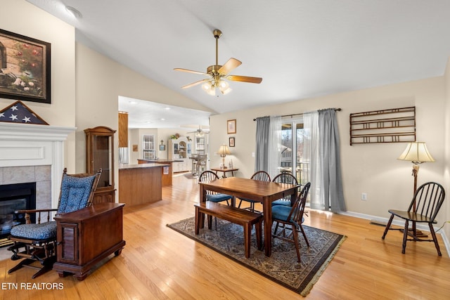 dining room featuring ceiling fan, a tile fireplace, lofted ceiling, and light hardwood / wood-style flooring