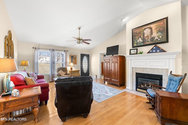 living room with ceiling fan, a tile fireplace, lofted ceiling, and light hardwood / wood-style flooring