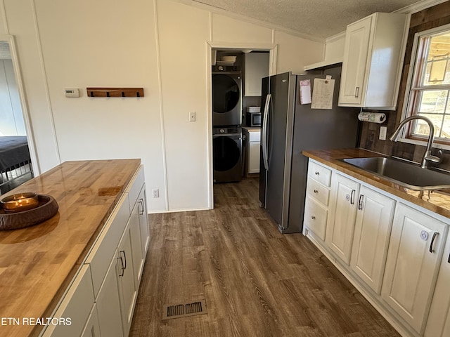 kitchen featuring sink, stacked washer / dryer, appliances with stainless steel finishes, a textured ceiling, and wood counters