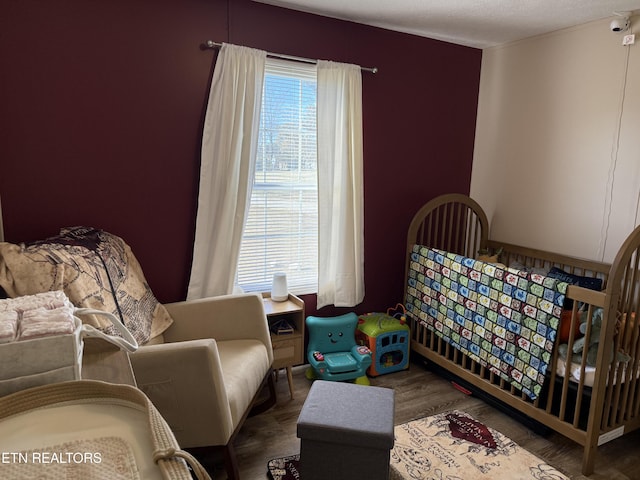 bedroom featuring dark wood-type flooring, a textured ceiling, and a nursery area