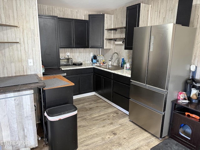 kitchen with light wood-type flooring, stainless steel fridge, sink, and wooden walls