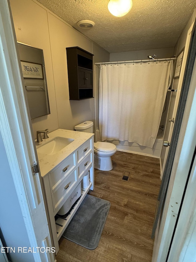 full bathroom featuring a textured ceiling, hardwood / wood-style floors, vanity, shower / tub combo, and toilet