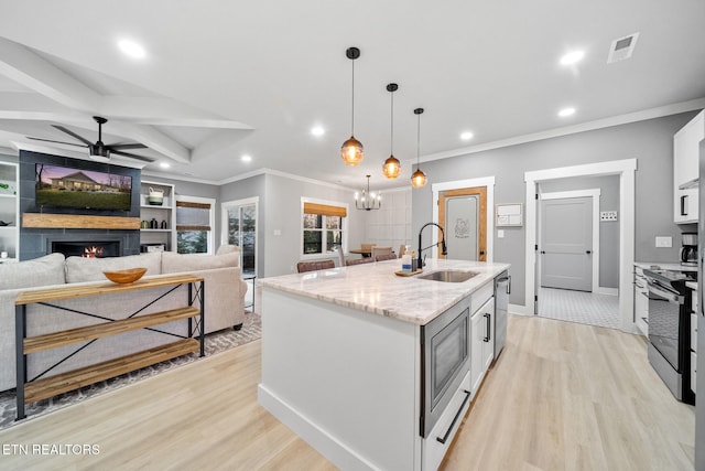 kitchen with light stone countertops, appliances with stainless steel finishes, an island with sink, sink, and hanging light fixtures