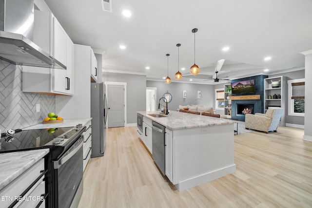 kitchen with white cabinetry, a center island with sink, stainless steel appliances, wall chimney range hood, and sink