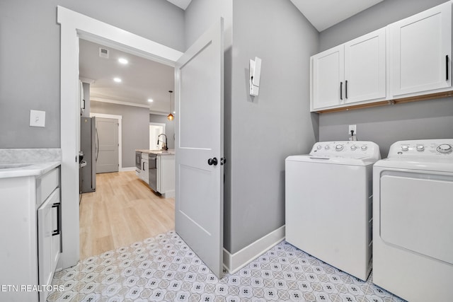 laundry area with cabinets, washer and dryer, light hardwood / wood-style flooring, and sink