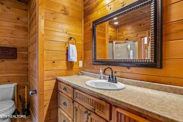 bathroom with vanity, wooden walls, a shower with shower door, and toilet