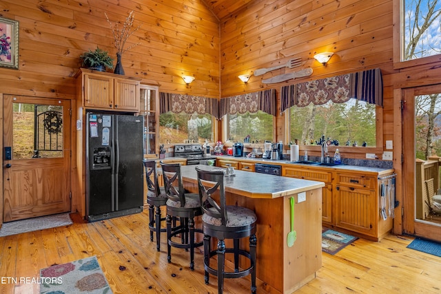 kitchen featuring sink, wood walls, a center island, high vaulted ceiling, and black appliances