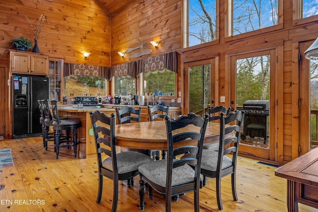 dining area featuring high vaulted ceiling, light hardwood / wood-style flooring, and wood walls