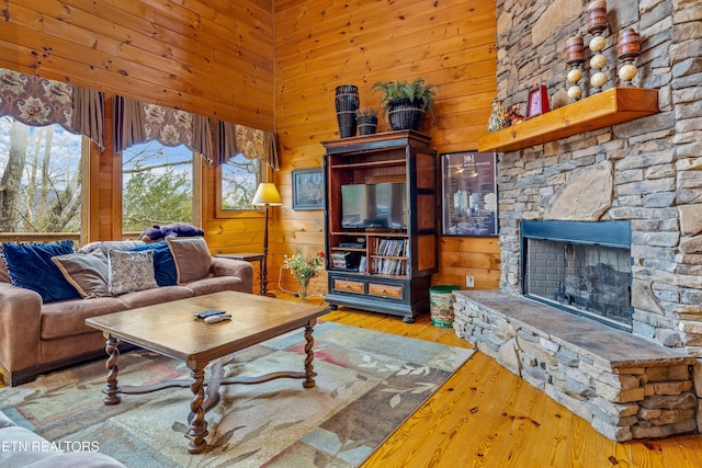 living room with a towering ceiling, a fireplace, light hardwood / wood-style floors, and wood walls