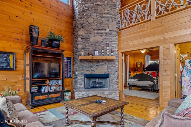 living room with a high ceiling, a fireplace, light wood-type flooring, and wood walls