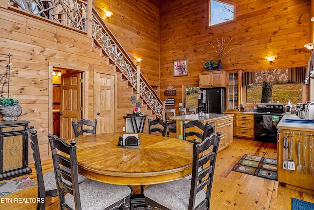 dining room with sink, a towering ceiling, wooden walls, and light hardwood / wood-style floors