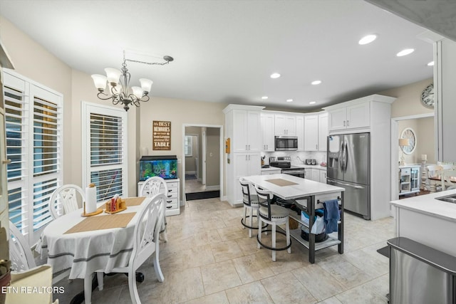 kitchen featuring tasteful backsplash, an inviting chandelier, white cabinetry, hanging light fixtures, and stainless steel appliances