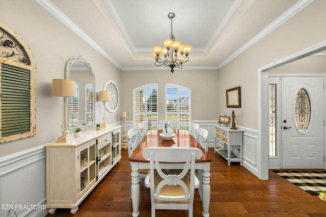 dining space featuring dark wood-type flooring, ornamental molding, an inviting chandelier, and a tray ceiling