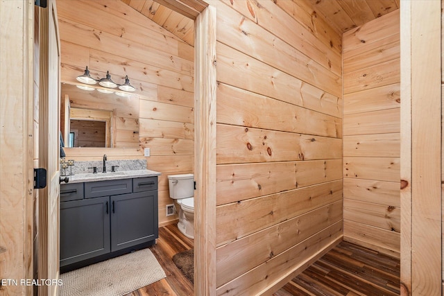 bathroom with toilet, vanity, wood-type flooring, and wood walls