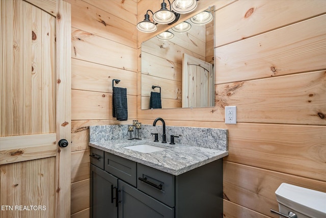 bathroom with toilet, vanity, and wood walls