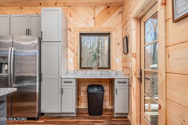 kitchen featuring stainless steel fridge, dark hardwood / wood-style floors, wood walls, gray cabinets, and light stone counters