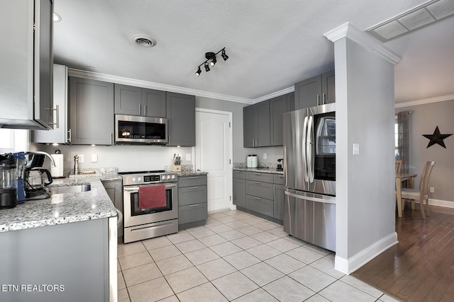 kitchen with light tile patterned flooring, ornamental molding, appliances with stainless steel finishes, and gray cabinetry