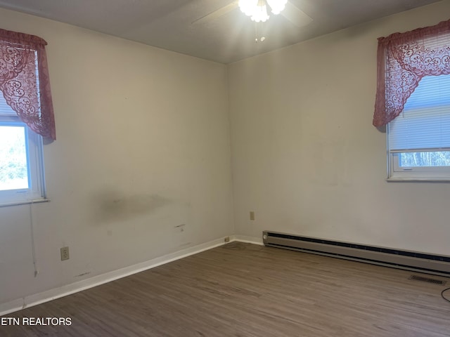 spare room featuring baseboard heating, ceiling fan, a healthy amount of sunlight, and dark hardwood / wood-style floors