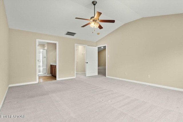 unfurnished bedroom featuring lofted ceiling, a walk in closet, light colored carpet, ensuite bath, and a closet