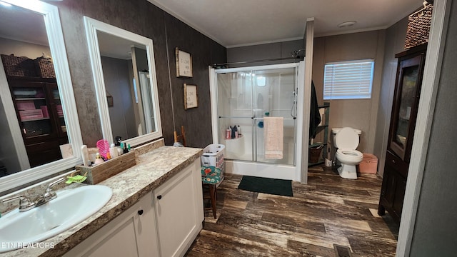 bathroom featuring toilet, vanity, wood-type flooring, ornamental molding, and an enclosed shower