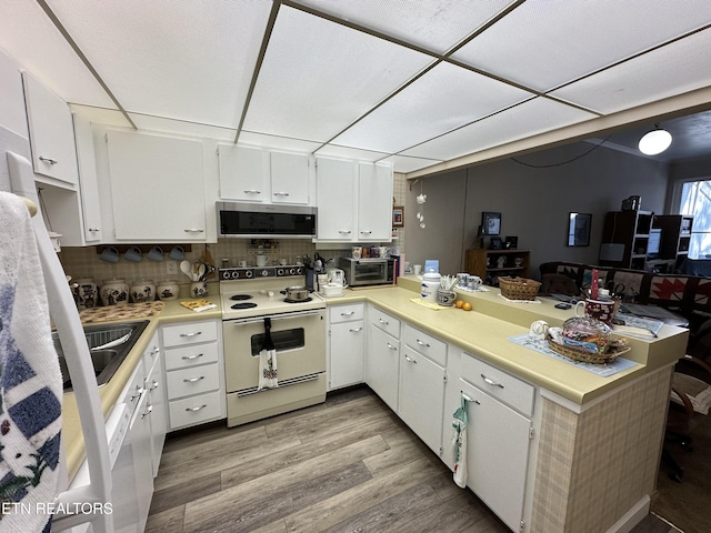 kitchen with white range with electric stovetop, kitchen peninsula, and white cabinets