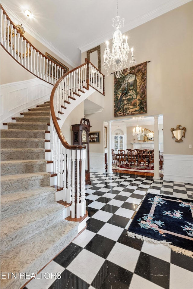 foyer entrance with decorative columns, ornamental molding, a high ceiling, and a notable chandelier