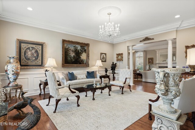 living room with dark wood-type flooring, an inviting chandelier, crown molding, and decorative columns