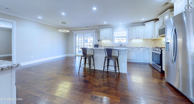 kitchen with light stone countertops, white cabinets, appliances with stainless steel finishes, a center island, and tasteful backsplash