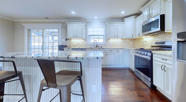 kitchen featuring a breakfast bar area, appliances with stainless steel finishes, light stone countertops, white cabinets, and sink