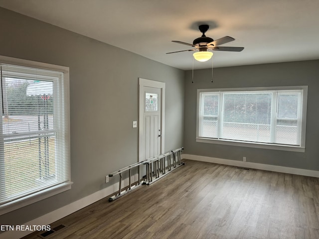 empty room featuring ceiling fan, a healthy amount of sunlight, and hardwood / wood-style floors