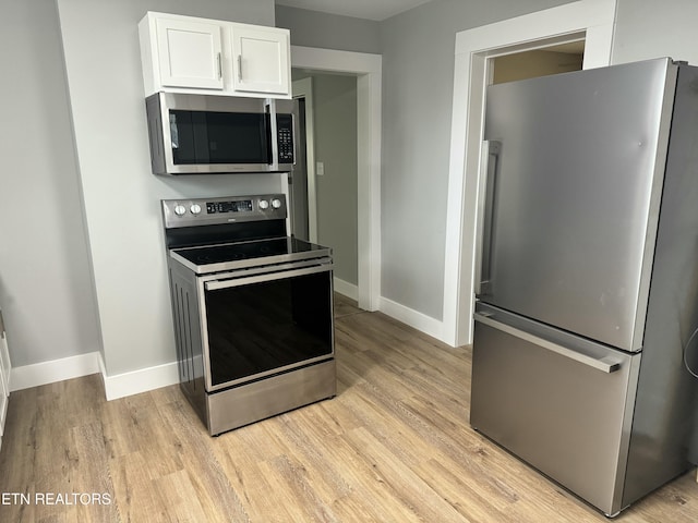 kitchen with white cabinets, light wood-type flooring, and appliances with stainless steel finishes