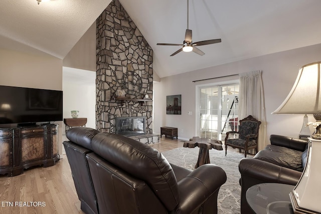 living room featuring a textured ceiling, a fireplace, light hardwood / wood-style floors, ceiling fan, and high vaulted ceiling