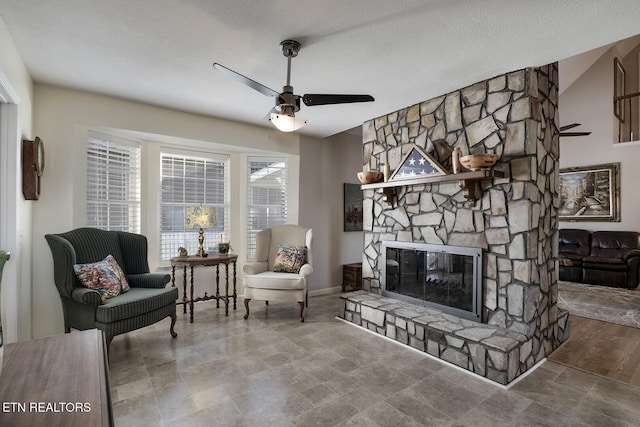 sitting room with ceiling fan, a textured ceiling, and a stone fireplace