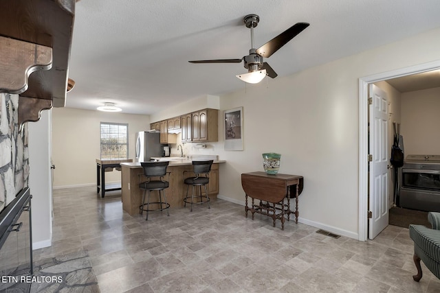 kitchen featuring stainless steel refrigerator, stove, sink, kitchen peninsula, and a breakfast bar