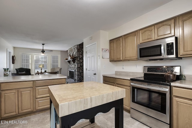 kitchen with ceiling fan, wooden counters, appliances with stainless steel finishes, a stone fireplace, and a kitchen island