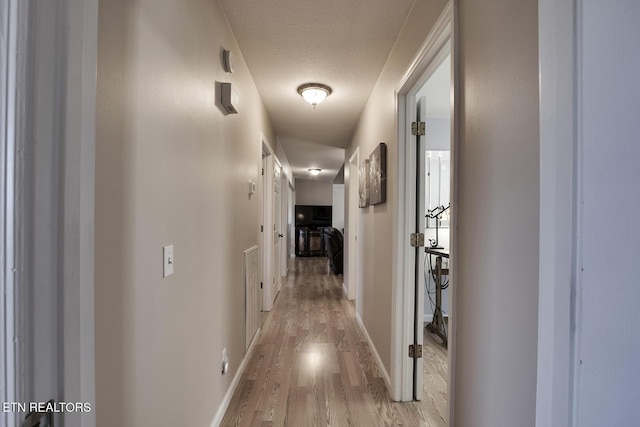 hall featuring a textured ceiling and light hardwood / wood-style flooring