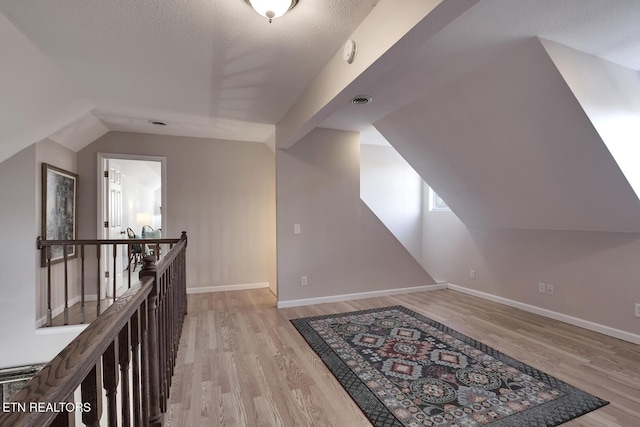 additional living space with light hardwood / wood-style floors, a textured ceiling, and lofted ceiling