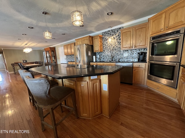 kitchen with hardwood / wood-style floors, decorative light fixtures, a kitchen island with sink, stainless steel appliances, and crown molding