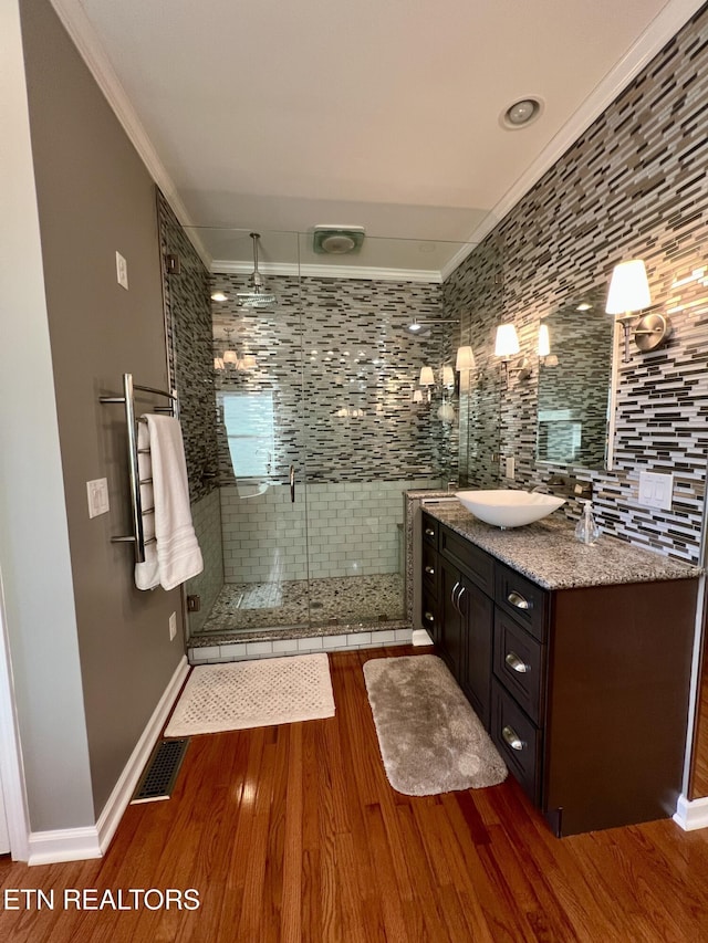 bathroom with a shower with shower door, ornamental molding, vanity, hardwood / wood-style floors, and backsplash