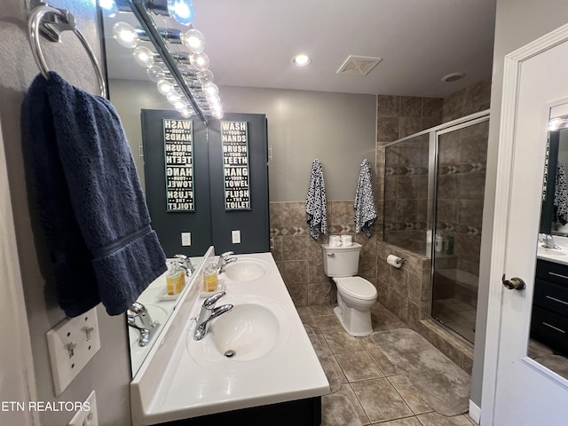 bathroom with tile patterned floors, toilet, a shower with shower door, tile walls, and vanity