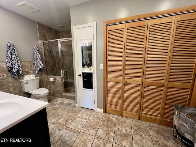 bathroom with a shower with door, tile walls, vanity, tile patterned floors, and toilet